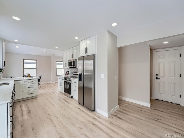 kitchen with stainless steel appliances, kitchen peninsula, light hardwood / wood-style floors, decorative backsplash, and white cabinets