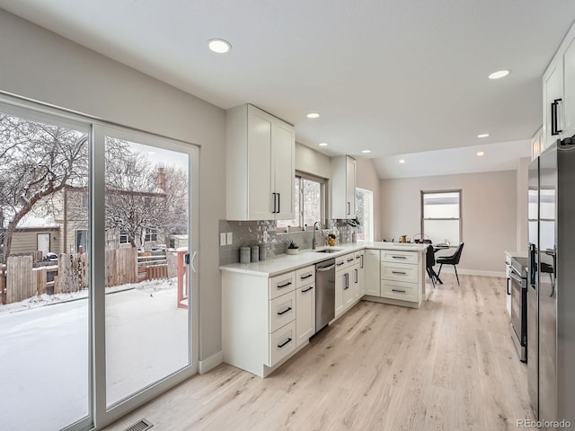 kitchen featuring kitchen peninsula, white cabinetry, light hardwood / wood-style flooring, and stainless steel appliances