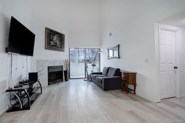 living room featuring a fireplace, light hardwood / wood-style floors, and a towering ceiling