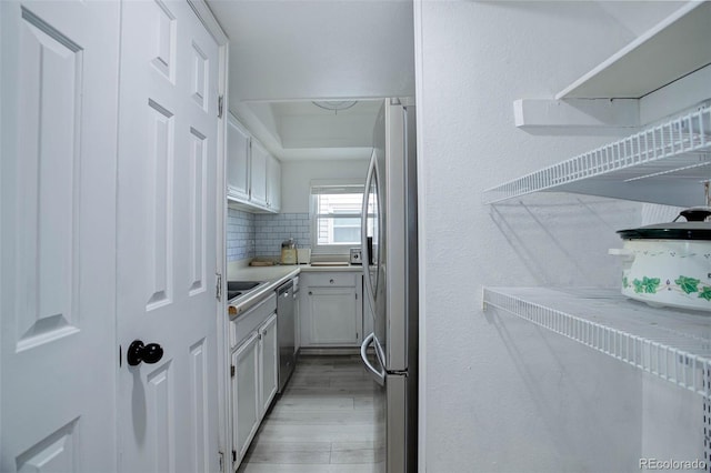 kitchen featuring stainless steel appliances, white cabinetry, light hardwood / wood-style floors, and backsplash