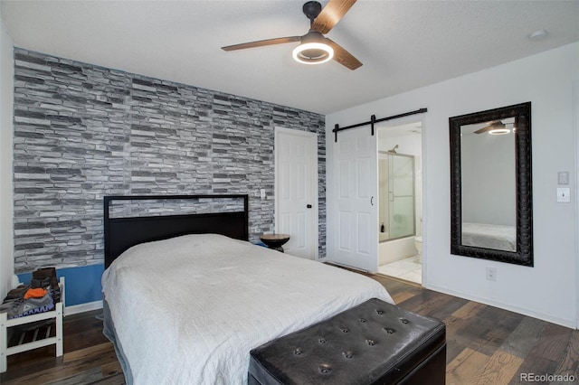 bedroom with a textured ceiling, dark hardwood / wood-style floors, ceiling fan, ensuite bathroom, and a barn door