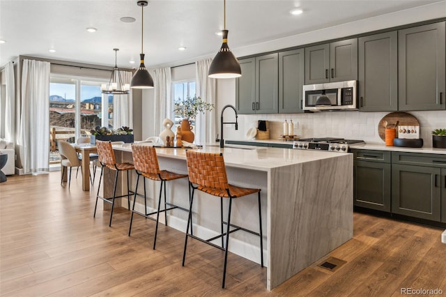 kitchen with stainless steel microwave, wood finished floors, a kitchen breakfast bar, a center island with sink, and backsplash