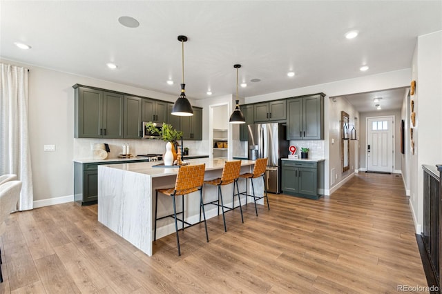 kitchen featuring light wood finished floors, stainless steel appliances, backsplash, and a center island with sink