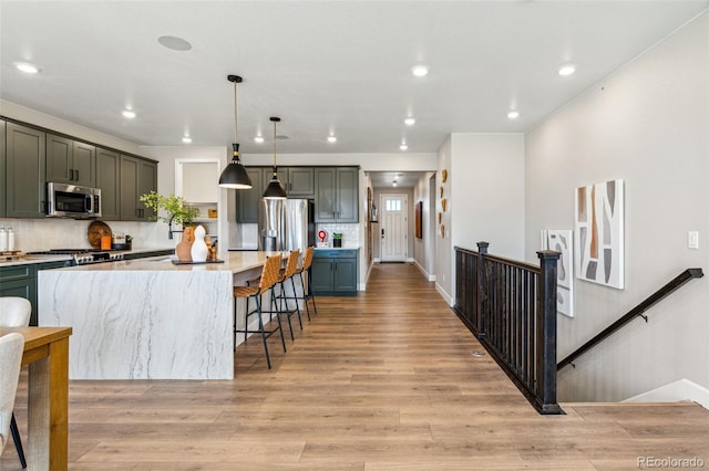 kitchen featuring a kitchen breakfast bar, a kitchen island, light wood-style floors, stainless steel appliances, and tasteful backsplash