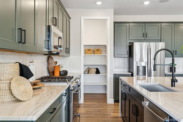 kitchen featuring a sink, stainless steel appliances, light stone counters, dark wood-type flooring, and backsplash