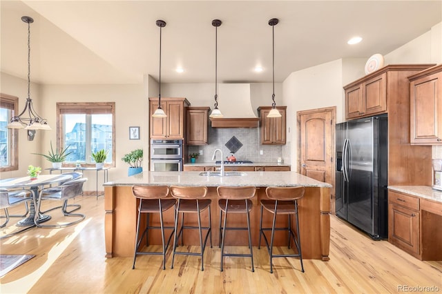 kitchen featuring an island with sink, hanging light fixtures, custom range hood, and appliances with stainless steel finishes