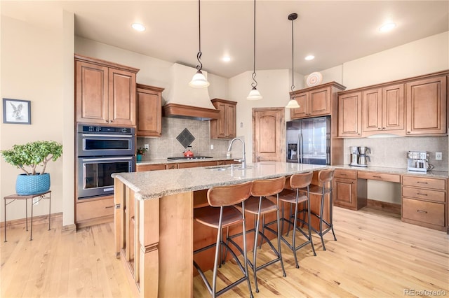 kitchen featuring a center island with sink, light stone counters, stainless steel appliances, and sink