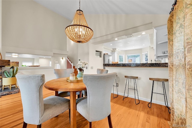 dining room featuring plenty of natural light, light wood-type flooring, a chandelier, high vaulted ceiling, and stairway