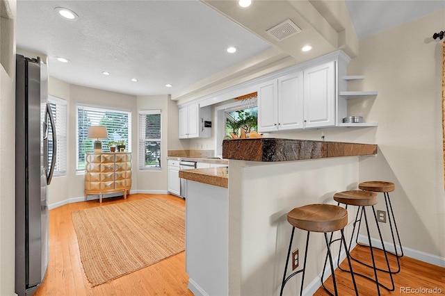 kitchen featuring freestanding refrigerator, white cabinets, a breakfast bar area, healthy amount of natural light, and recessed lighting