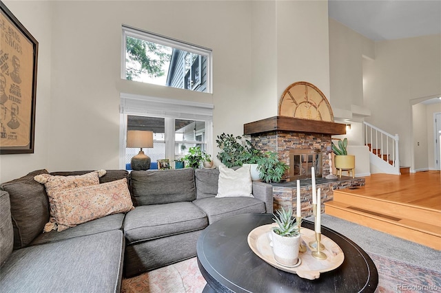 living area with a towering ceiling, plenty of natural light, a stone fireplace, stairs, and arched walkways