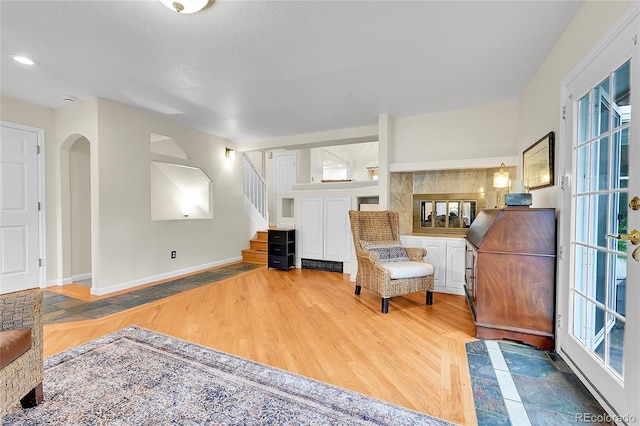 living area with stairway, baseboards, light wood-type flooring, and arched walkways