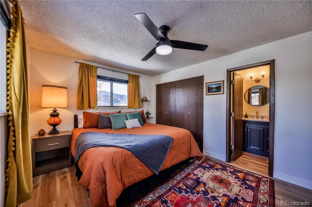 bedroom with a textured ceiling, ensuite bathroom, wood-type flooring, and ceiling fan