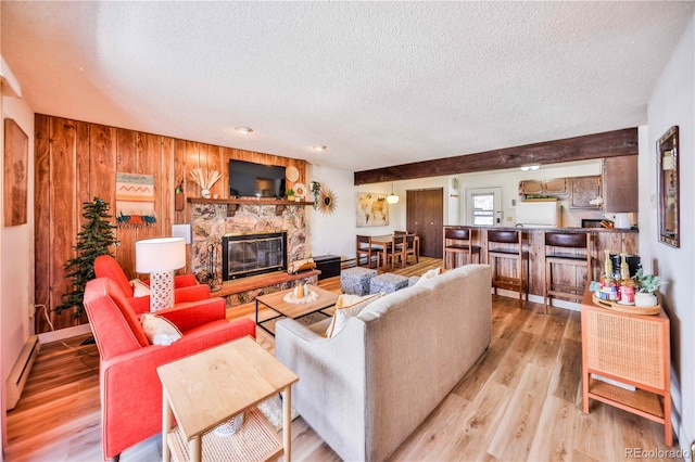 living room featuring baseboard heating, light hardwood / wood-style flooring, a stone fireplace, and a textured ceiling