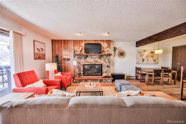 living room featuring beamed ceiling, hardwood / wood-style floors, a stone fireplace, and a textured ceiling