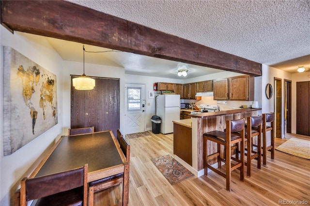 kitchen featuring kitchen peninsula, a kitchen bar, light hardwood / wood-style flooring, white fridge, and decorative light fixtures