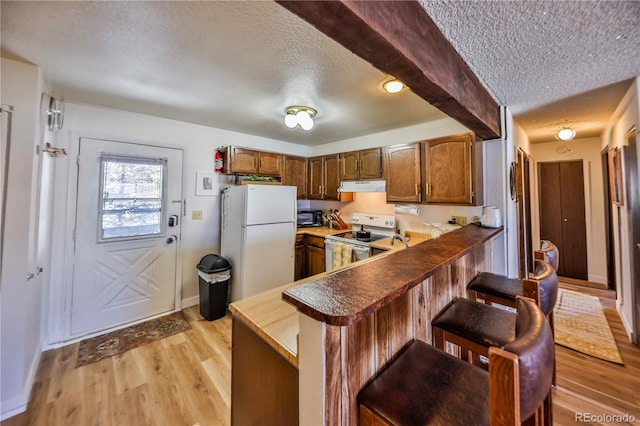 kitchen featuring white appliances, light wood-type flooring, a textured ceiling, kitchen peninsula, and a breakfast bar area