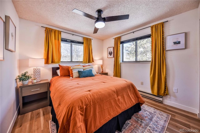 bedroom with hardwood / wood-style flooring, ceiling fan, multiple windows, and a baseboard radiator