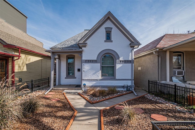 view of front of house featuring brick siding, roof with shingles, and fence