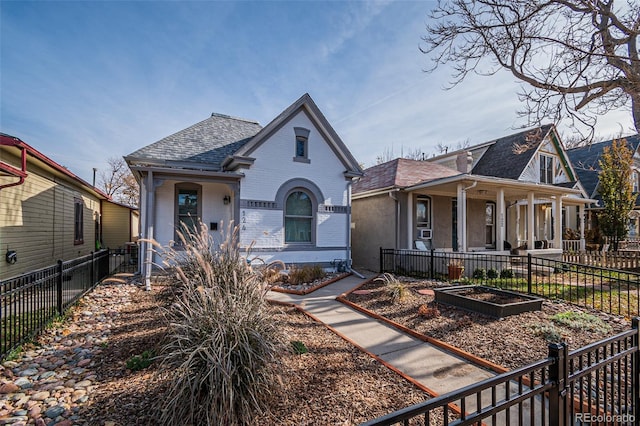 view of front of home with a porch, brick siding, fence, roof with shingles, and a vegetable garden