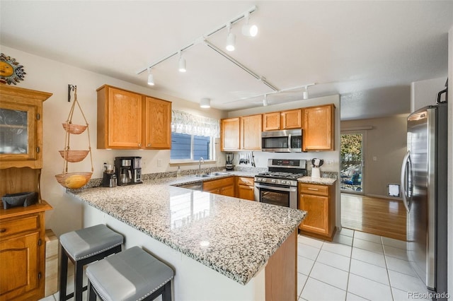 kitchen with light stone countertops, sink, stainless steel appliances, a kitchen breakfast bar, and kitchen peninsula