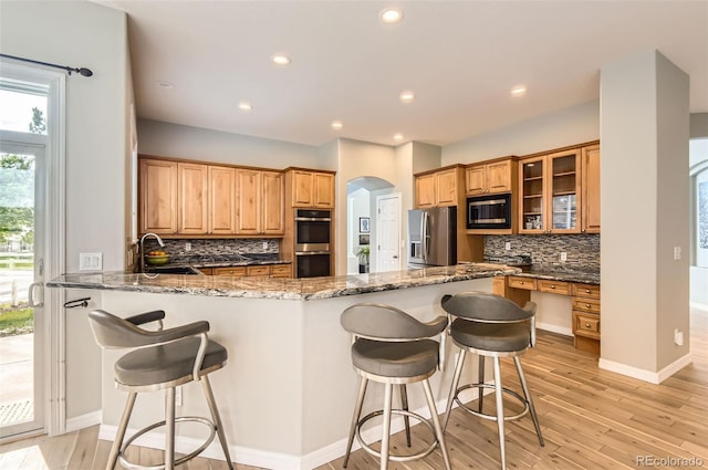 7866 Witney Pl, Lone Tree, CO 80124 - kitchen featuring appliances with stainless steel finishes, arched walkways, backsplash, glass insert cabinets, and dark stone counters