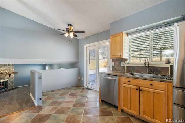 kitchen featuring stainless steel appliances, ceiling fan, sink, a fireplace, and tile counters