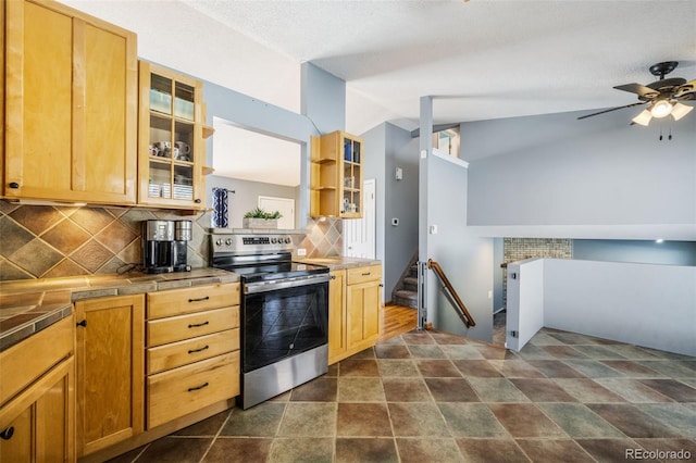 kitchen featuring tile countertops, backsplash, vaulted ceiling, ceiling fan, and stainless steel electric range oven