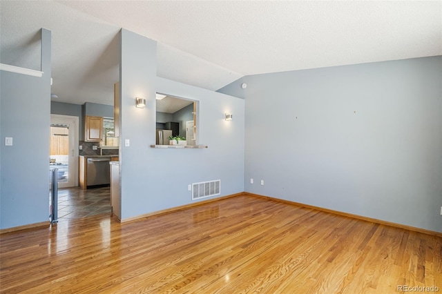 empty room featuring a textured ceiling, light hardwood / wood-style floors, and lofted ceiling