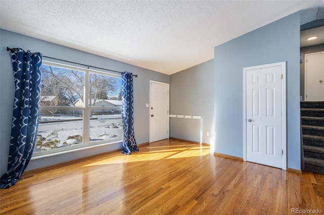 spare room featuring hardwood / wood-style floors, lofted ceiling, and a textured ceiling