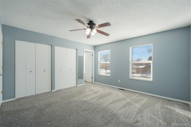 unfurnished bedroom with multiple closets, ceiling fan, light colored carpet, and a textured ceiling