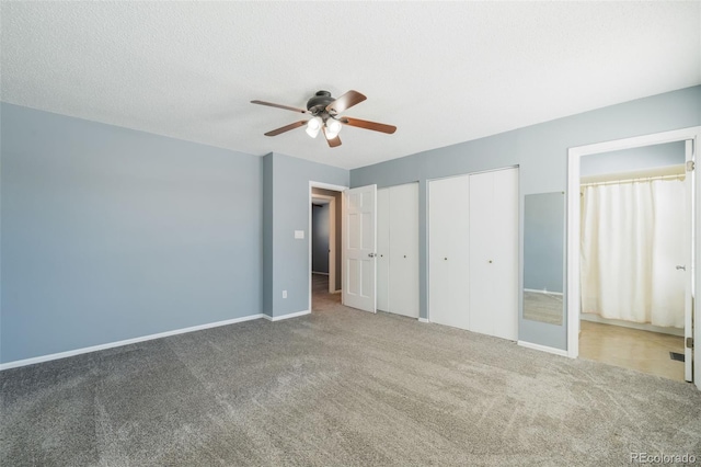 unfurnished bedroom with a textured ceiling, carpet floors, two closets, and ceiling fan