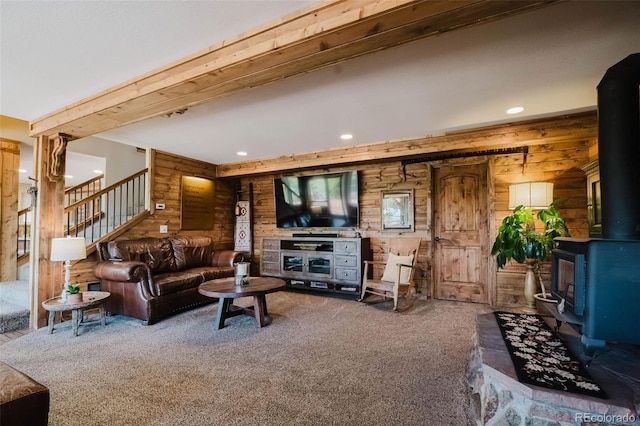 living room with a wood stove, carpet, wooden walls, recessed lighting, and stairs