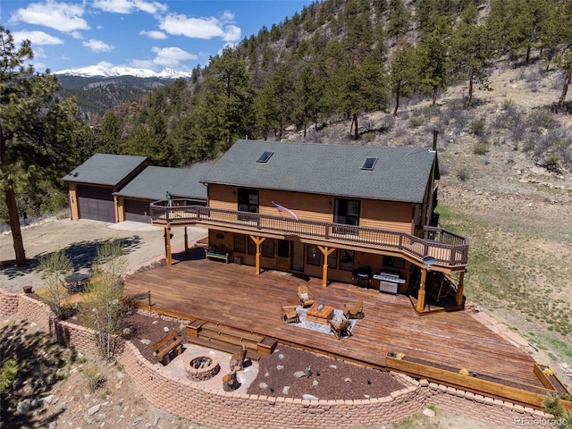 rear view of house with a fire pit, a deck with mountain view, a garage, and a view of trees