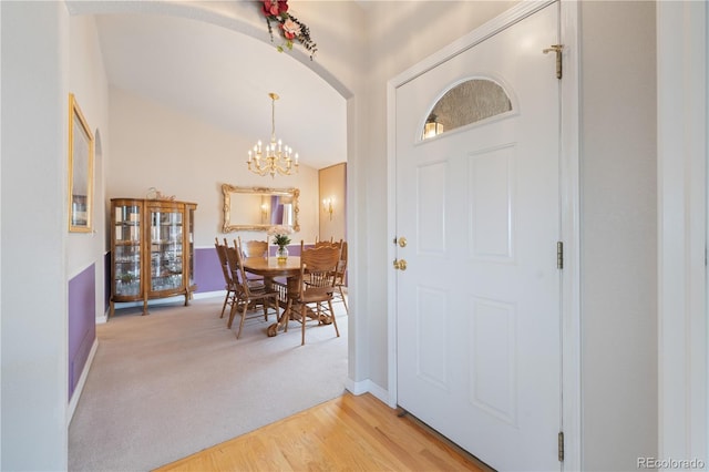 foyer entrance with baseboards, arched walkways, light wood-style floors, a notable chandelier, and light colored carpet