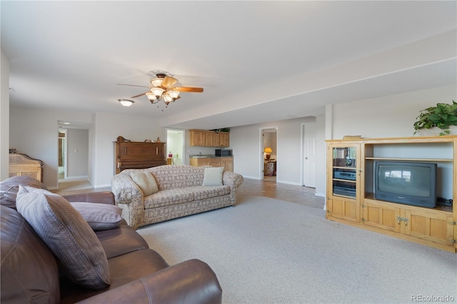 living area with baseboards, light carpet, and ceiling fan