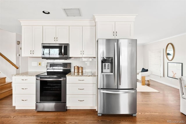 kitchen with stainless steel appliances, wood finished floors, visible vents, white cabinetry, and light stone countertops