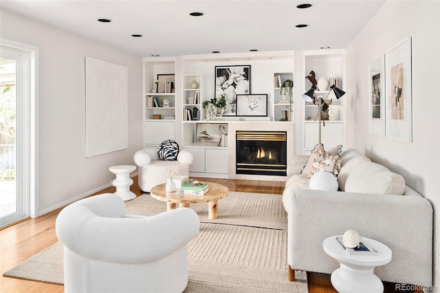 living area with recessed lighting, baseboards, wood finished floors, and a glass covered fireplace