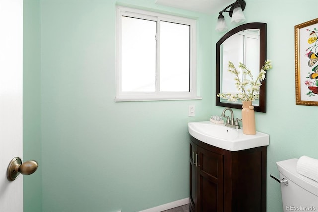 half bathroom with baseboards, vanity, and toilet