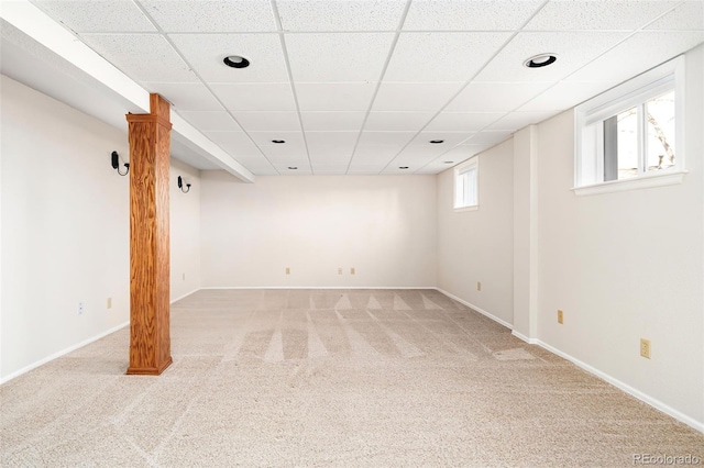 basement featuring a paneled ceiling, a healthy amount of sunlight, light carpet, and baseboards