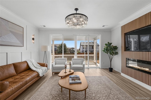 living room with a notable chandelier, a glass covered fireplace, visible vents, crown molding, and wood finished floors