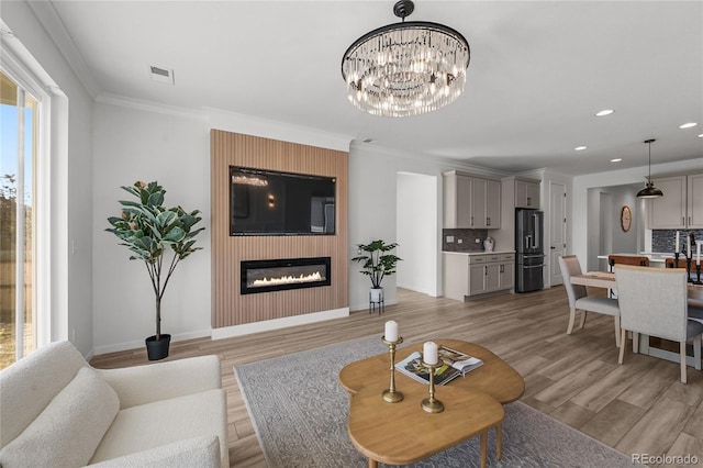 living area with recessed lighting, an inviting chandelier, light wood-style flooring, baseboards, and a glass covered fireplace