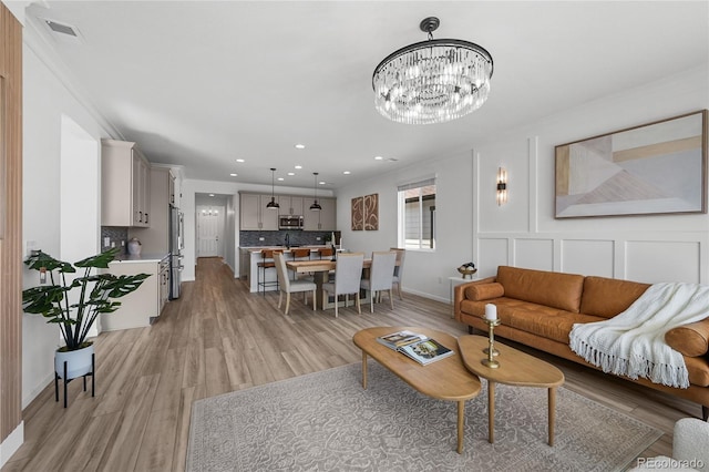 living area featuring a notable chandelier, visible vents, baseboards, light wood-style floors, and recessed lighting