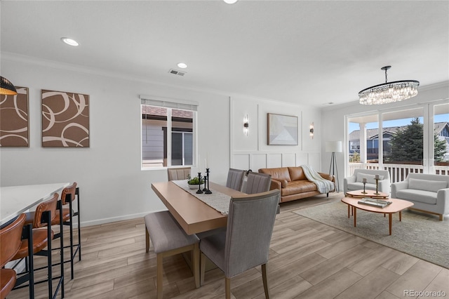 dining space featuring ornamental molding, a chandelier, light wood-type flooring, and plenty of natural light