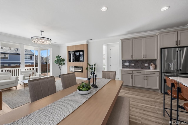dining area featuring ornamental molding, recessed lighting, a chandelier, light wood-style flooring, and a glass covered fireplace