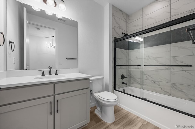 bathroom with toilet, wood finished floors, vanity, visible vents, and combined bath / shower with glass door