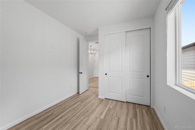 unfurnished bedroom with light wood finished floors, an inviting chandelier, a closet, and baseboards