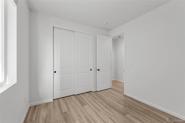unfurnished bedroom with baseboards, a closet, and light wood-type flooring