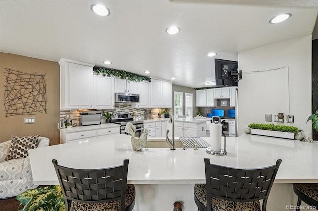 7548 S Biloxi Way, Aurora, CO 80016 - kitchen with stainless steel appliances, a kitchen breakfast bar, a peninsula, white cabinets, and tasteful backsplash