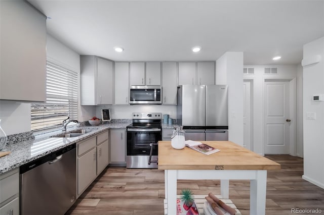 kitchen with light stone counters, sink, light wood-type flooring, and appliances with stainless steel finishes