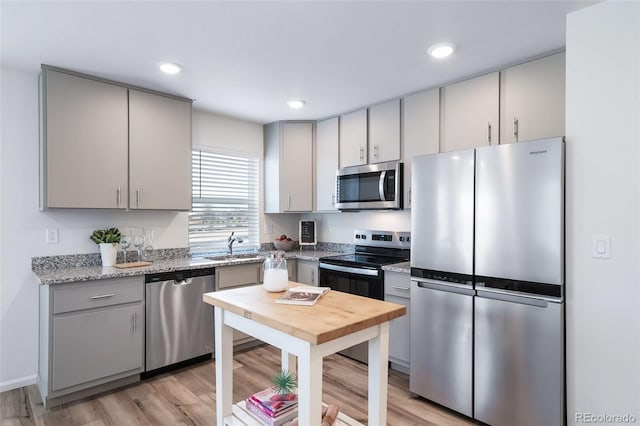 kitchen with light stone countertops, sink, light hardwood / wood-style floors, gray cabinets, and appliances with stainless steel finishes